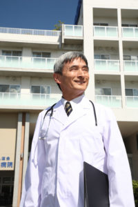病院の前に立つベテランの男性医師